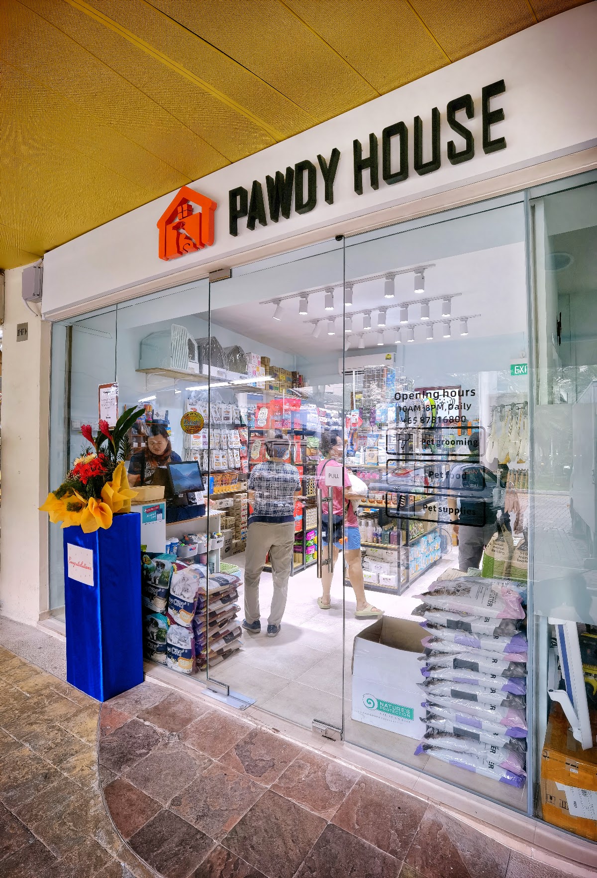The Pawdy House shopfront at Compassvale North Gate, glass doors open with a customer at the counter
