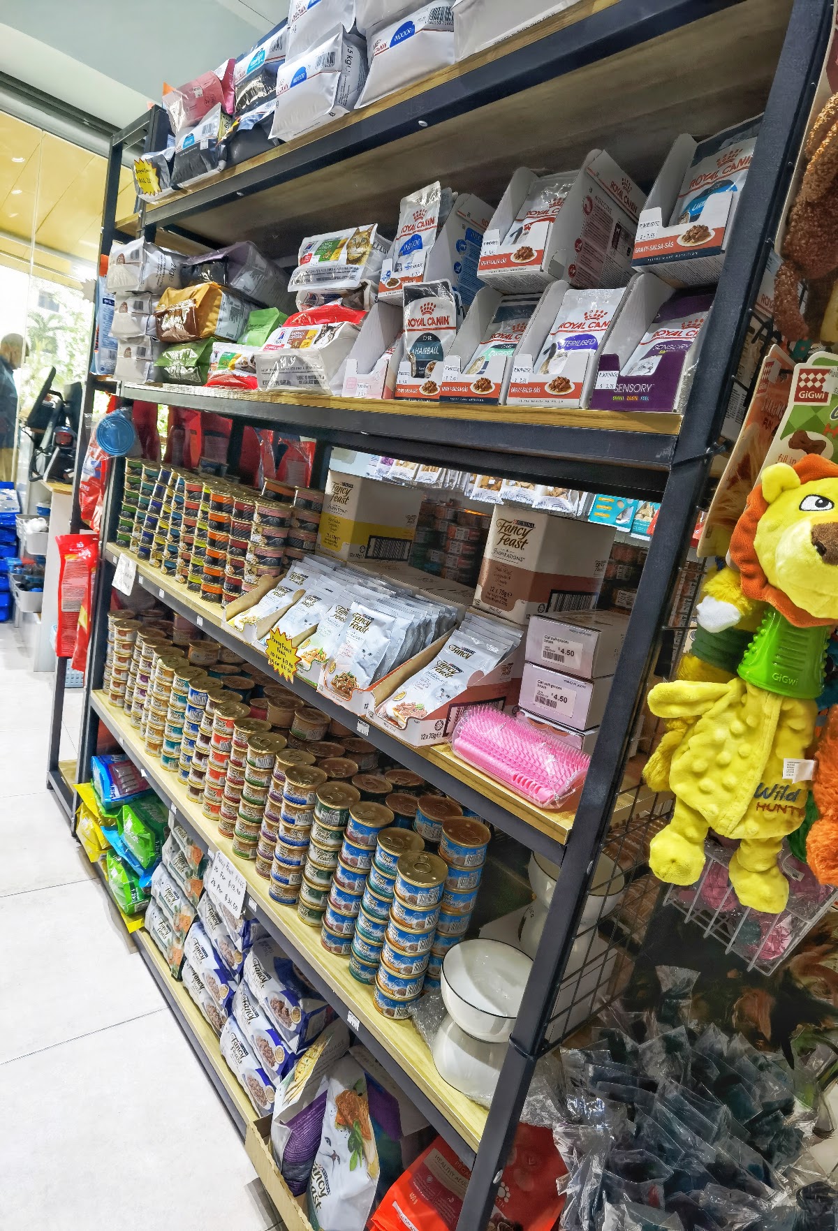 Retail shelving stacked with cat food tins, pouches and a plush lion toy