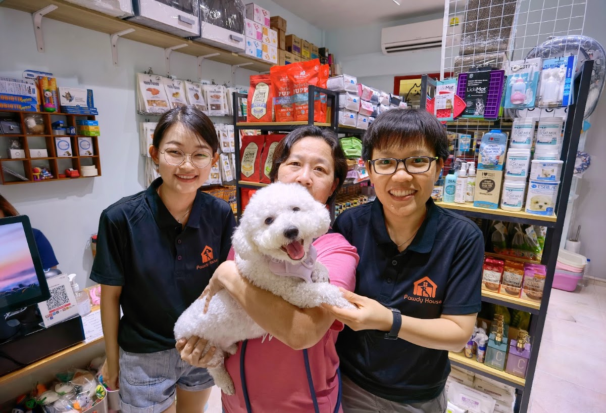 Three members of the Pawdy House team holding a white bichon in the shop